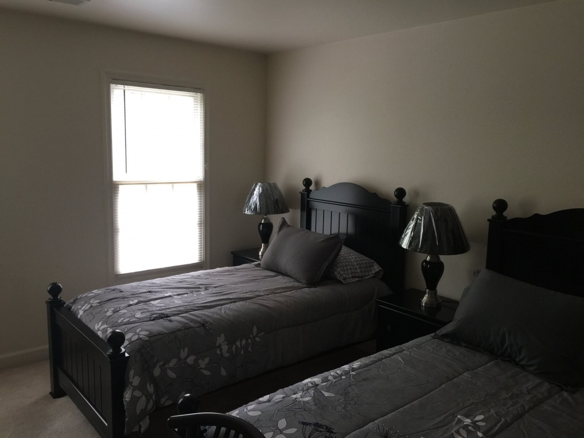 A bedroom with two twin beds and matching lamps beside a window.