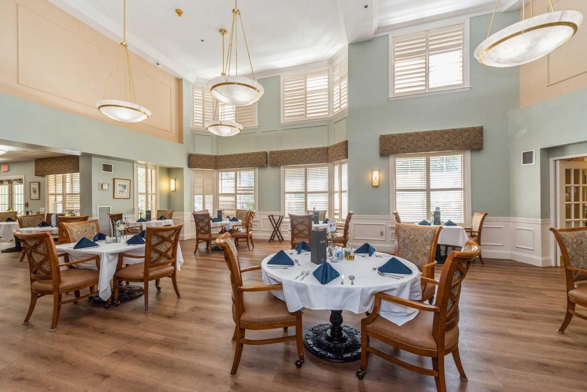 A spacious and elegant dining room with well-arranged tables and chairs, featuring large windows that allow natural light to brighten the space.