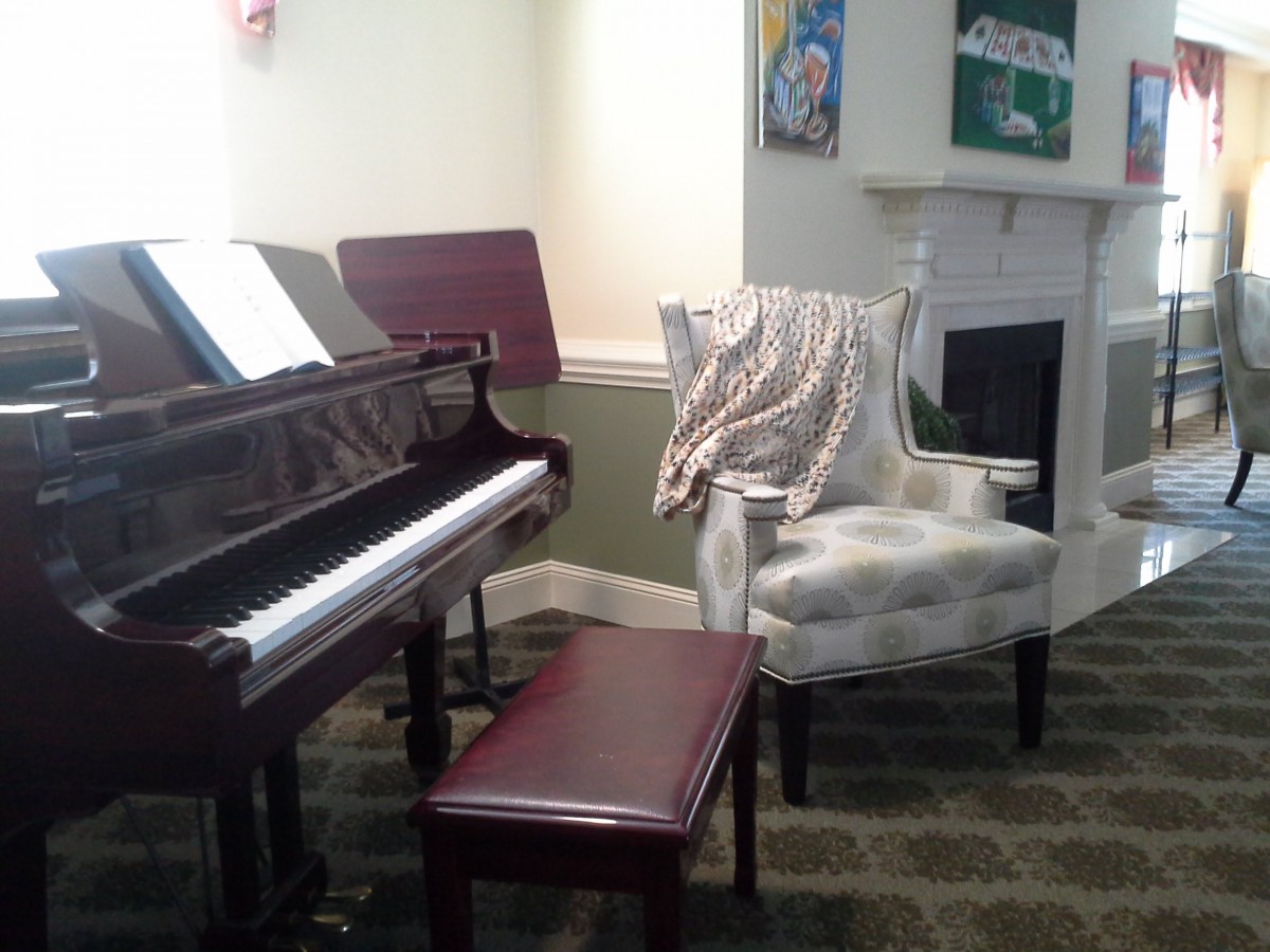 A cozy music room with a piano, chair, and artwork on the walls.