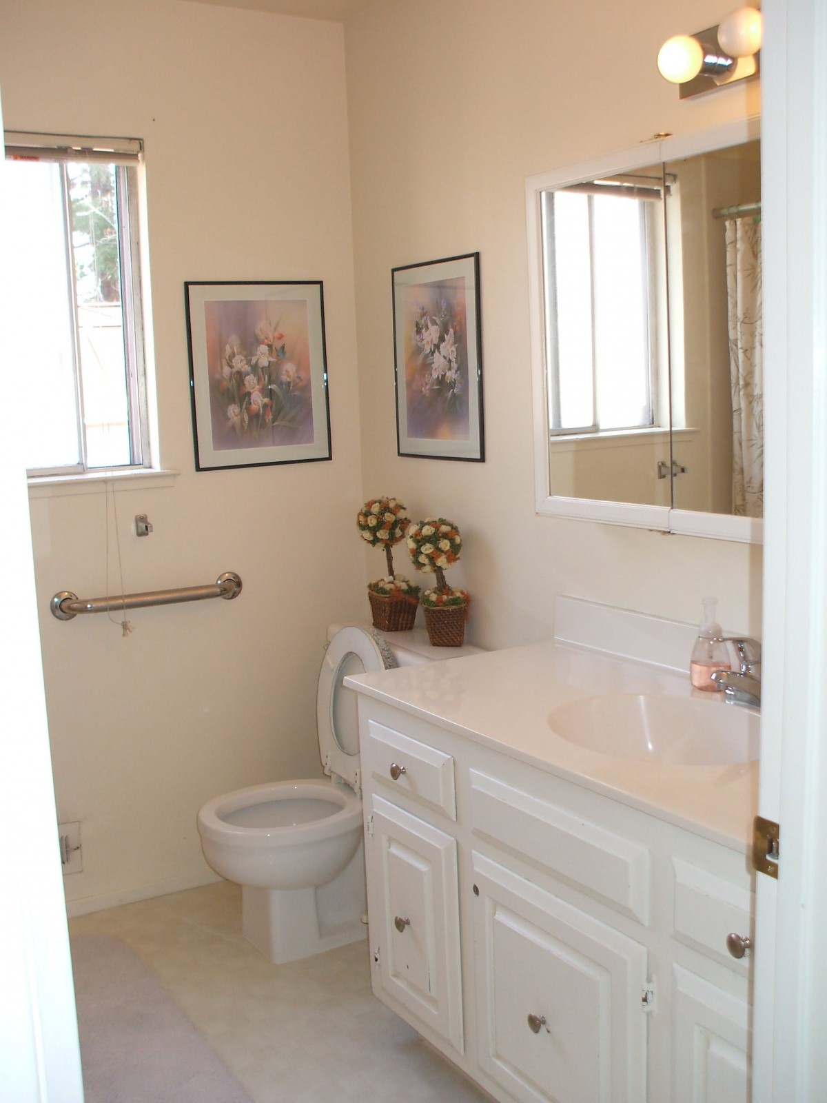 A small bathroom with a sink, toilet, mirror, and decorative wall art.