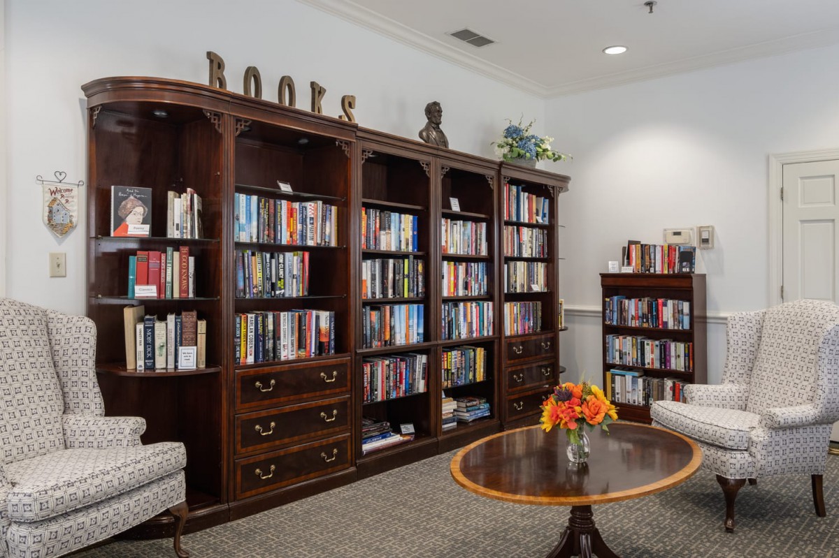 A cozy library reading room with wooden bookshelves filled with books and comfortable seating.
