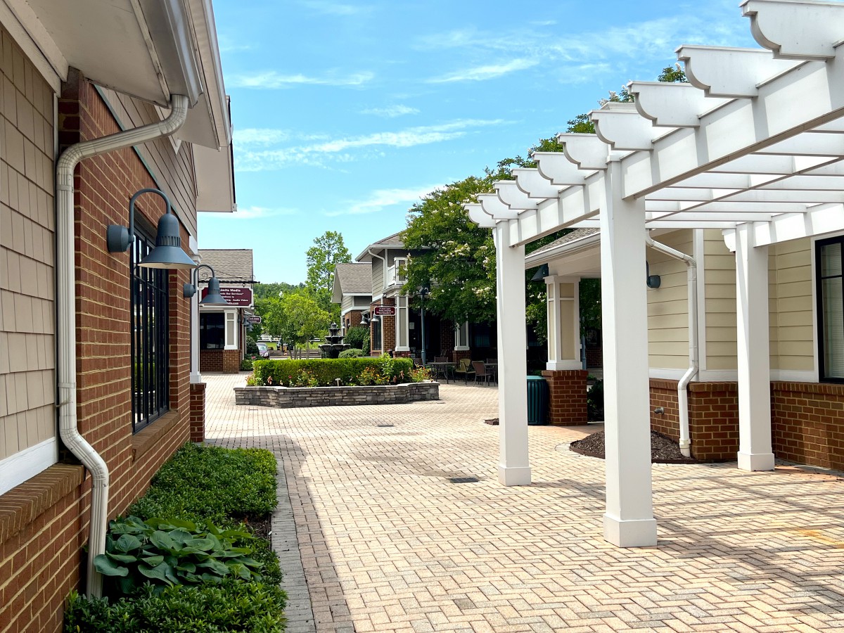 A sunny day at a charming outdoor shopping center with brick buildings and a white pergola.