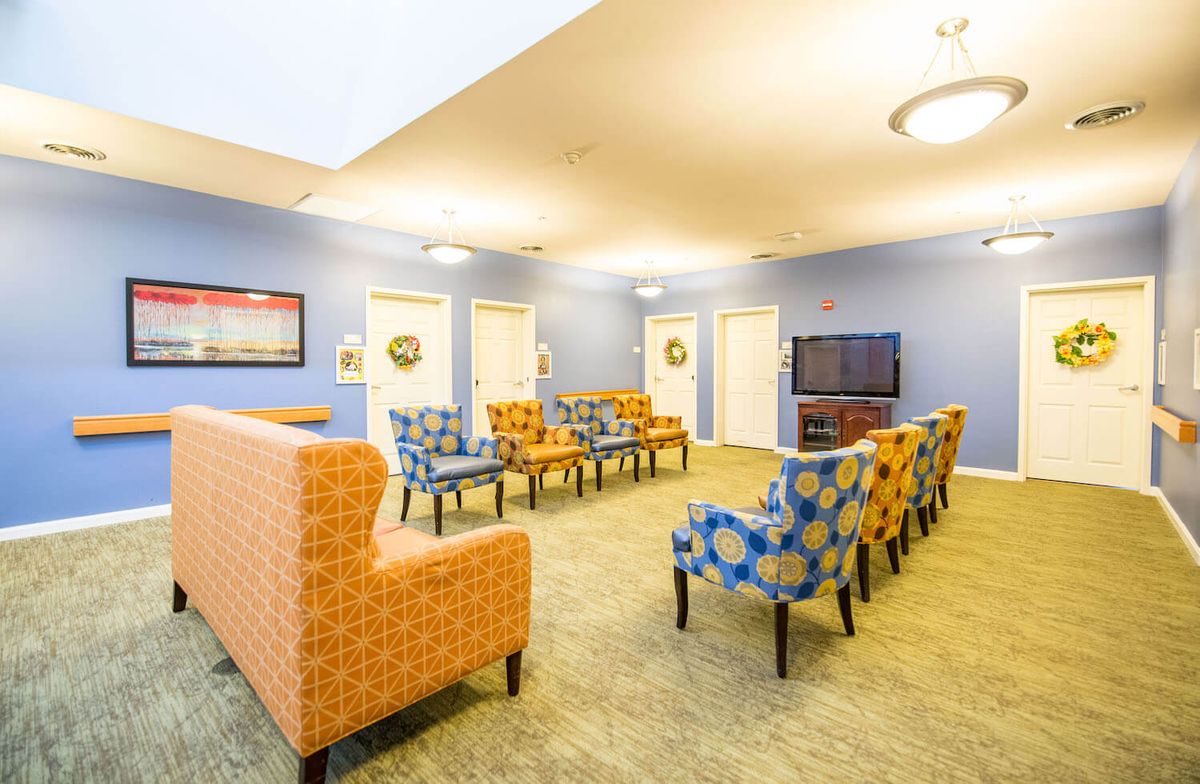A brightly lit living room with colorful chairs arranged in front of a television, set against blue walls.