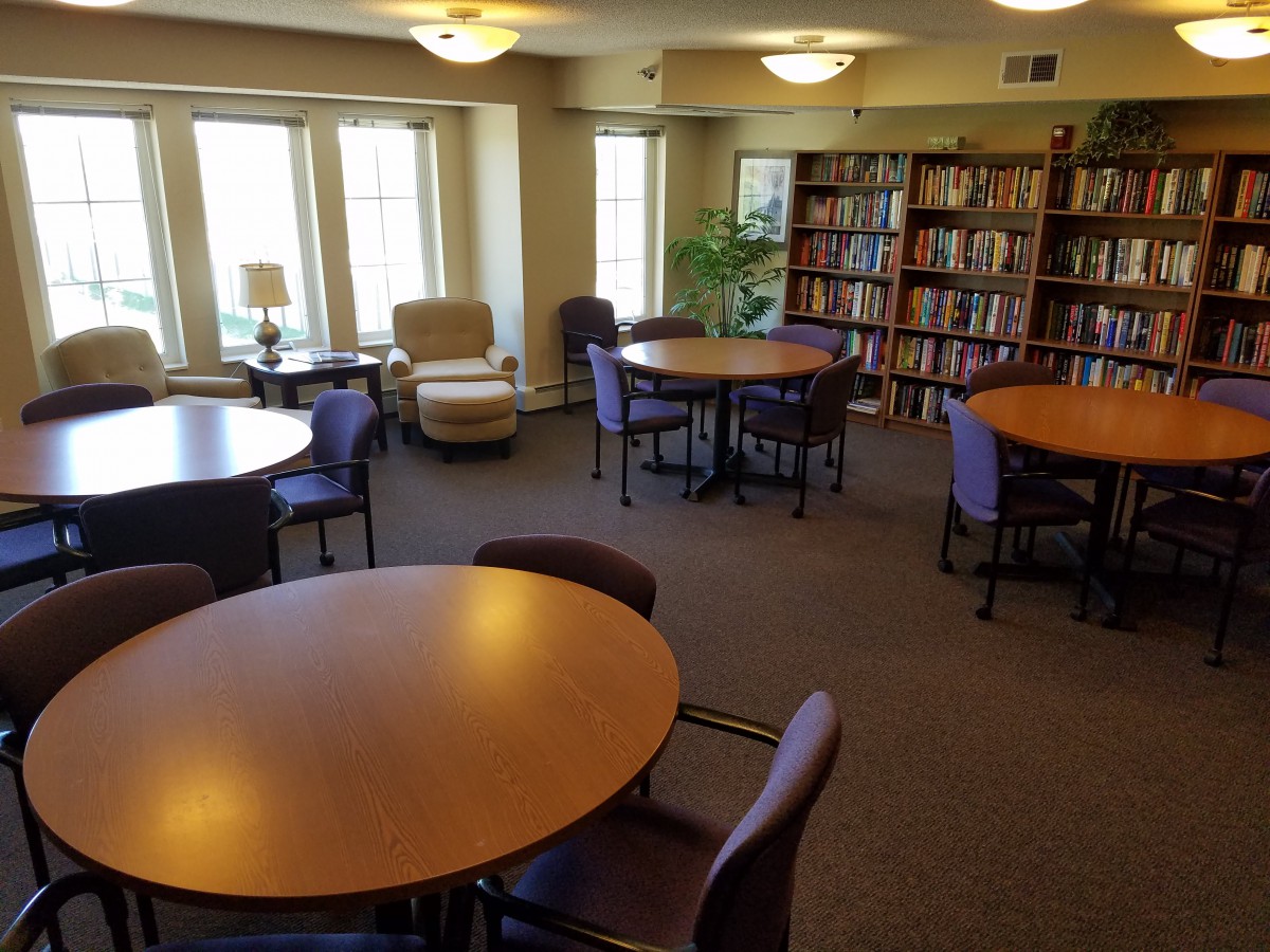 A quiet library reading room with tables, chairs, and bookshelves.