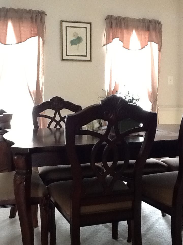 A cozy dining room with a wooden table and chairs, illuminated by natural light from the windows.