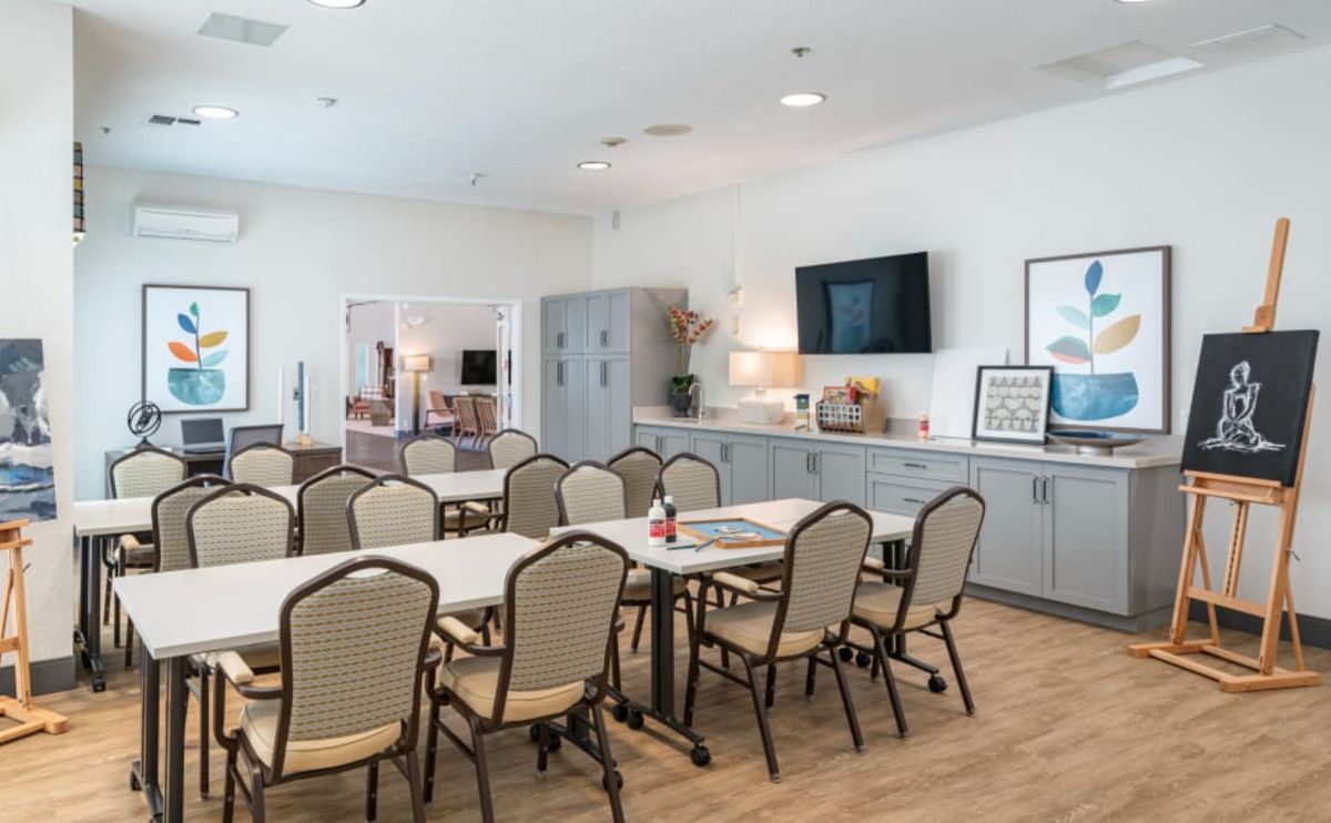 A modern meeting room with tables and chairs arranged for a conference, featuring a television and stylish decor.