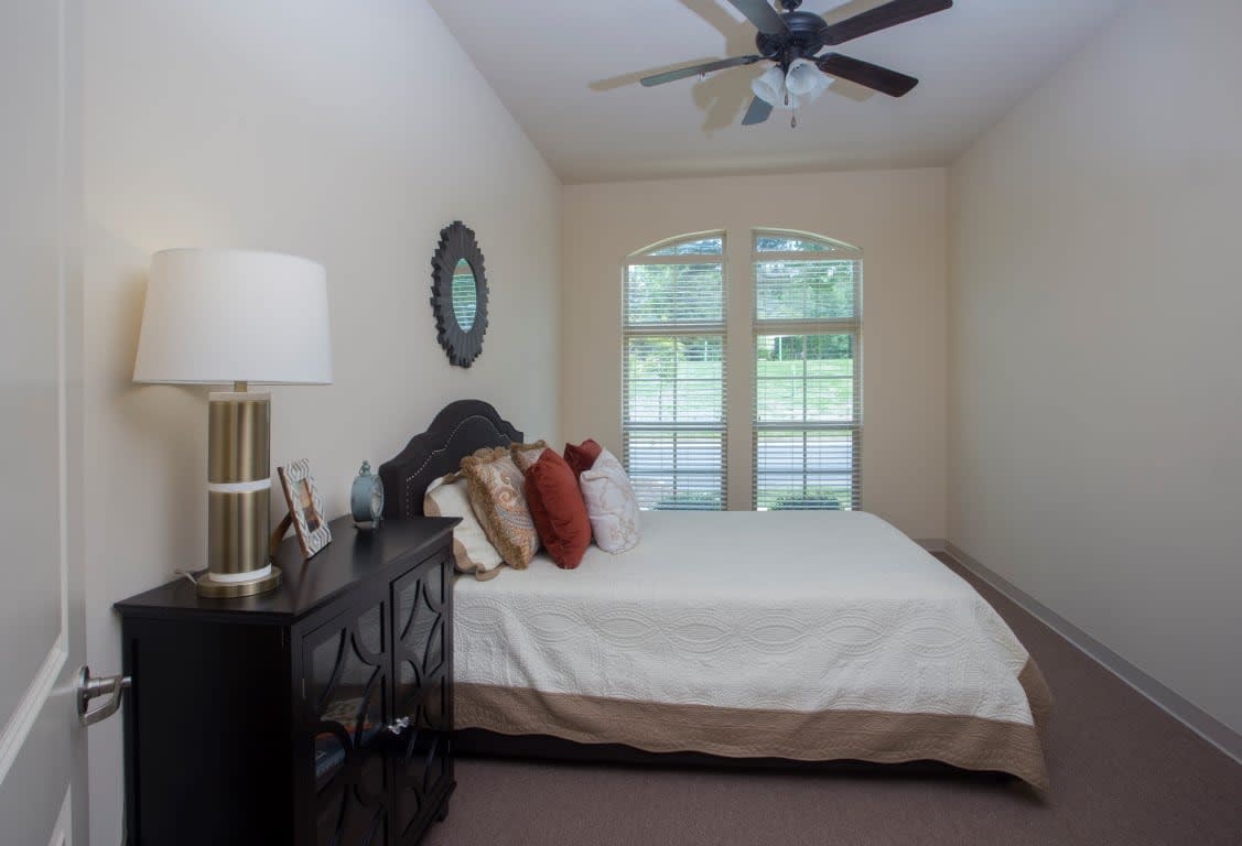 A cozy bedroom with a neatly made bed, decorative pillows, and ample natural light from large windows.