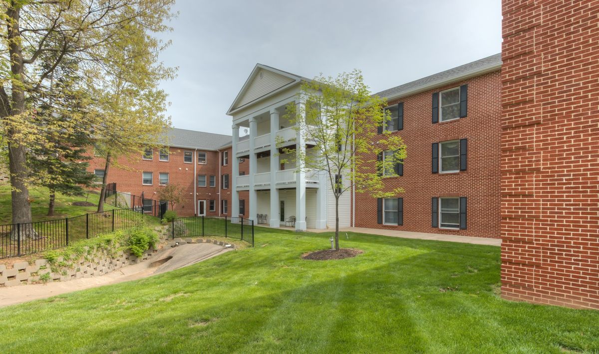 A view of a residential apartment building with brick exterior, surrounded by green grass and trees.