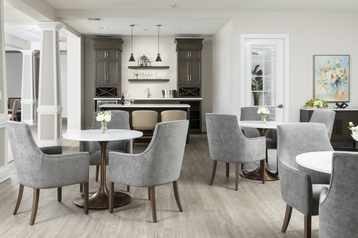 A modern and minimalist cafe interior with gray chairs and round tables, featuring a bar area in the background.