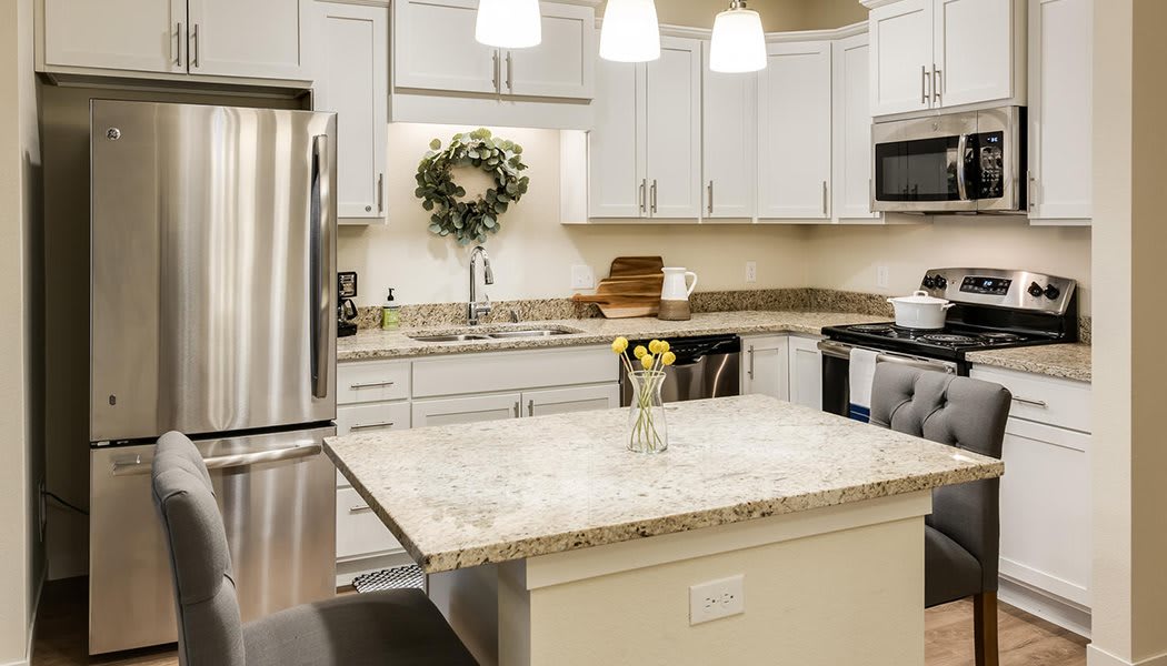 A modern kitchen with white cabinets, a granite island, and stainless steel appliances.