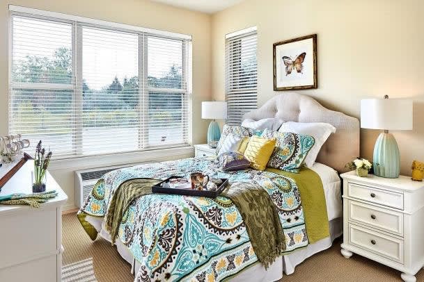A cozy bedroom with colorful paisley-patterned bedding and an array of decorative pillows, illuminated by natural light through large windows.