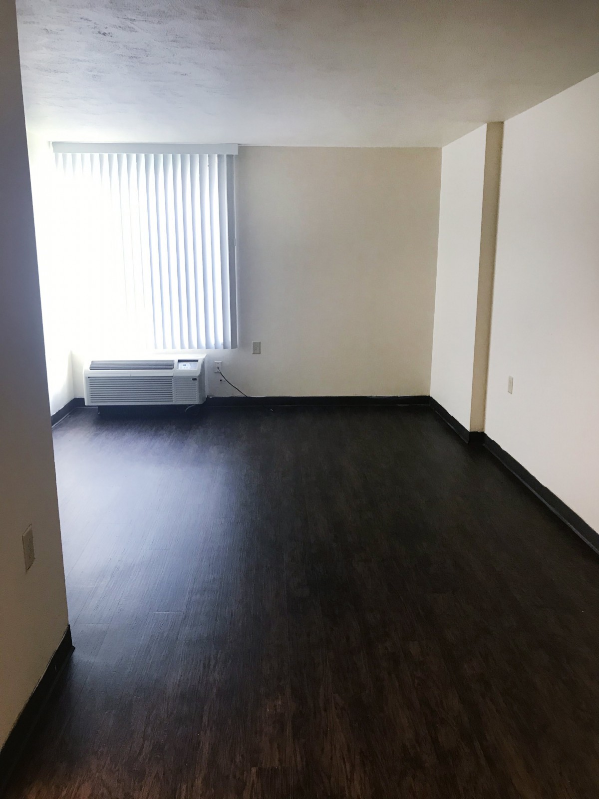 An empty room with hardwood floors and a large window offering natural light.