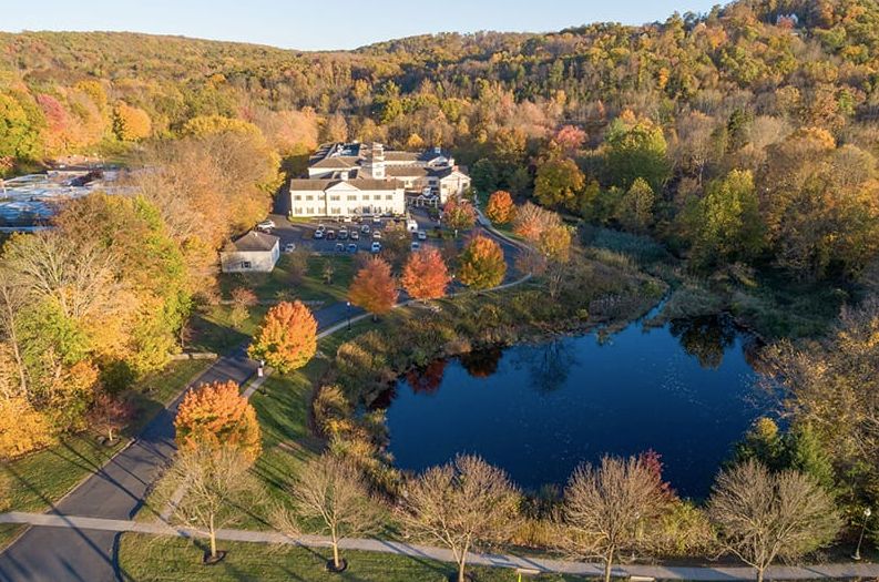 A picturesque aerial view of an estate surrounded by autumn foliage and a tranquil lake.