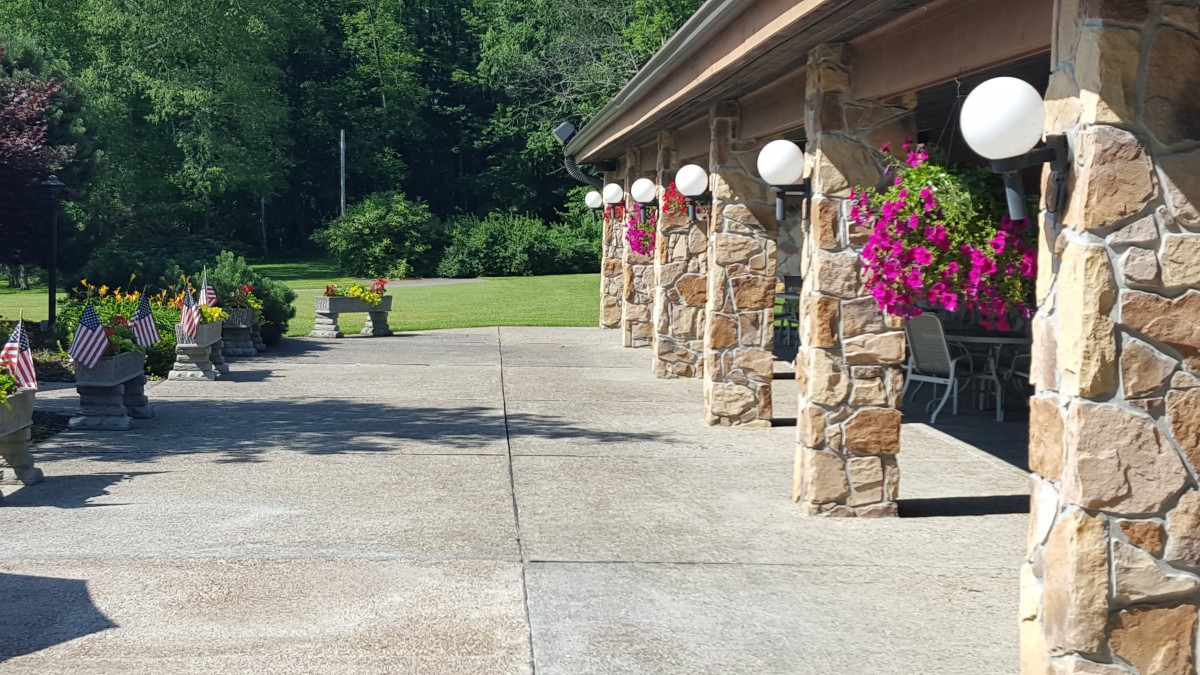A sunny outdoor patio with stone pillars, hanging flower baskets, and a nearby garden bench.
