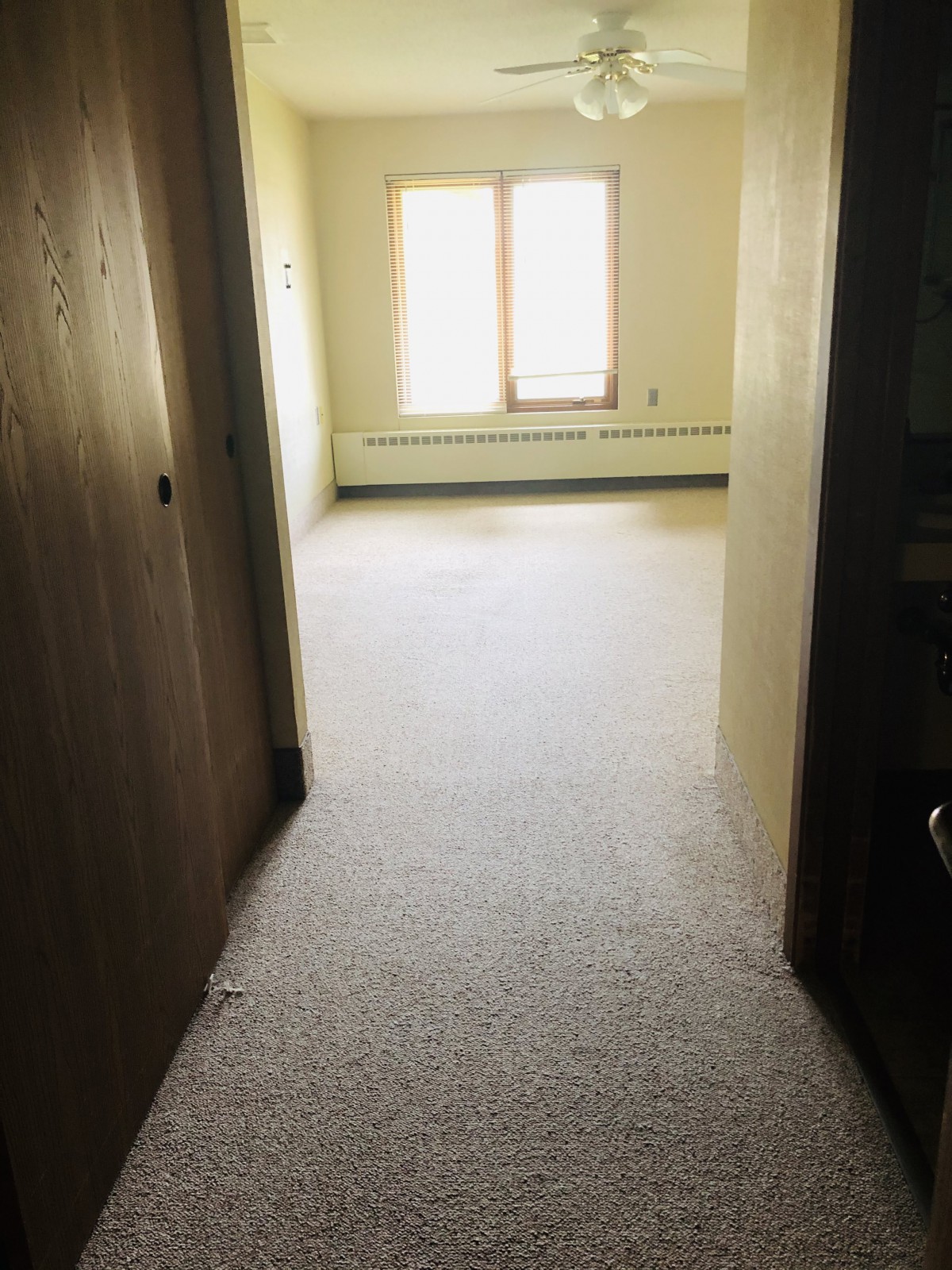 An empty room with carpet and two windows at the end of a hallway.