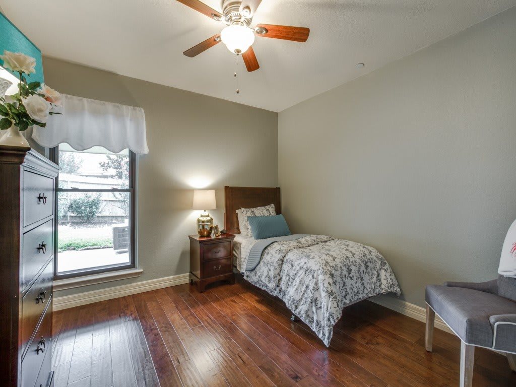A cozy bedroom with a single bed, wooden floors, and a ceiling fan.