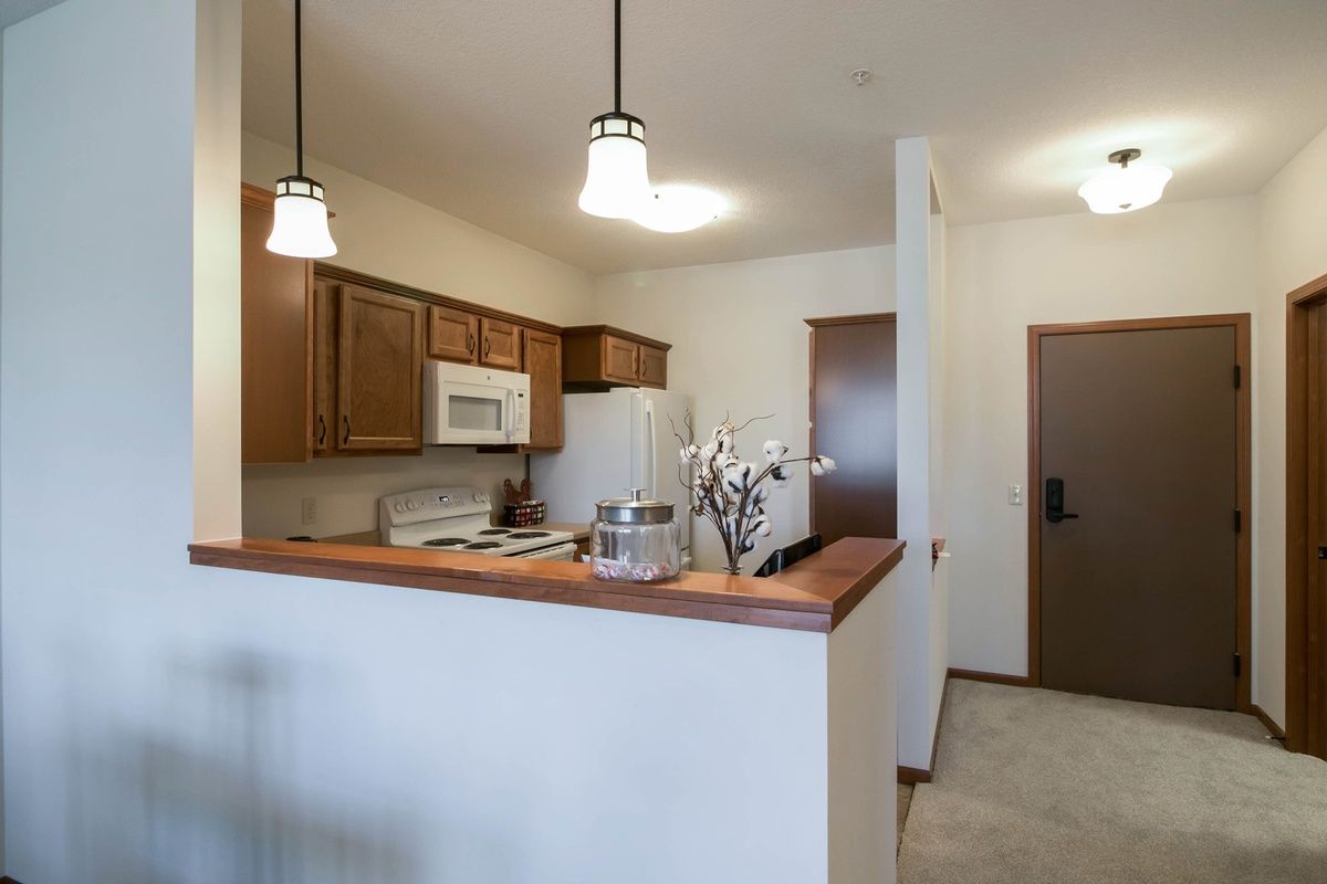 A modern kitchen interior with wooden cabinets, white appliances, and pendant lighting.