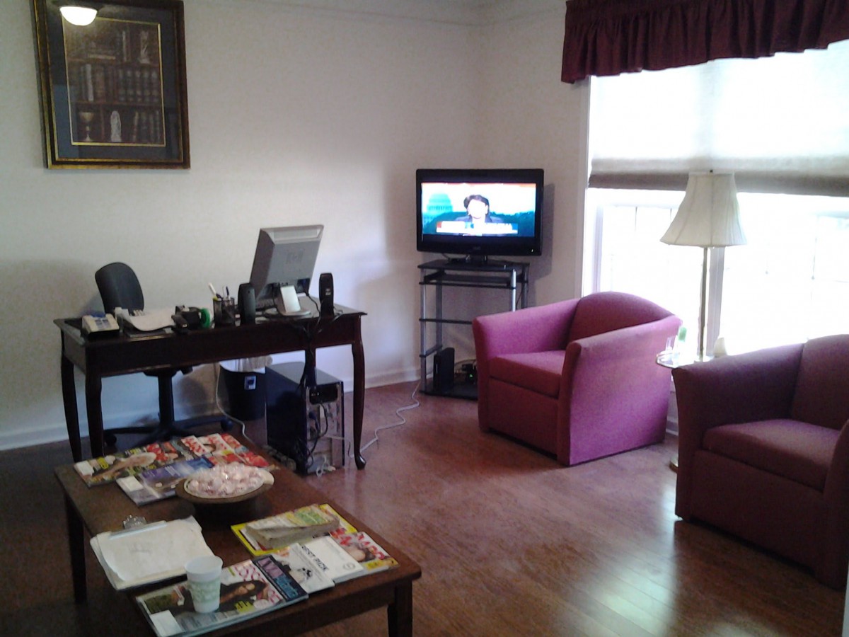 A cozy waiting room with a television, armchairs, and a desk.