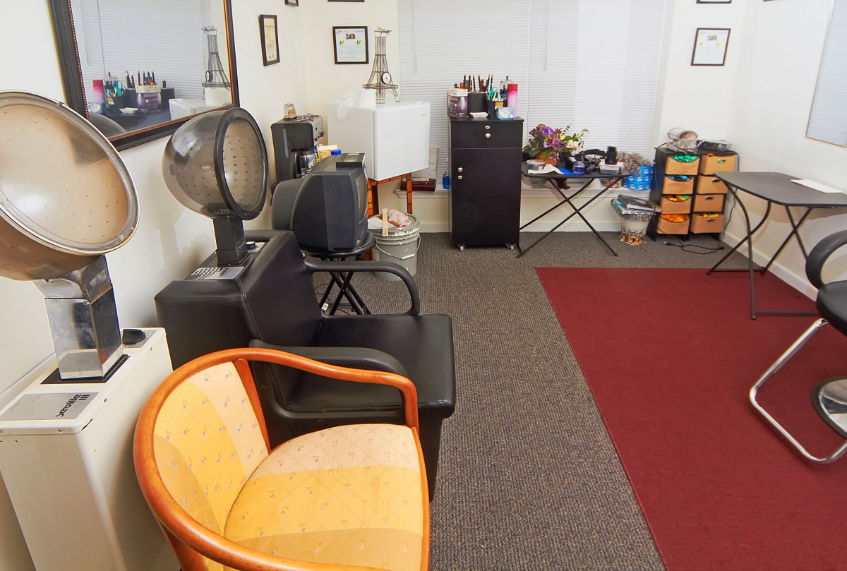 A cozy salon interior featuring a seating area with chairs, a hair dryer, and a mirror.