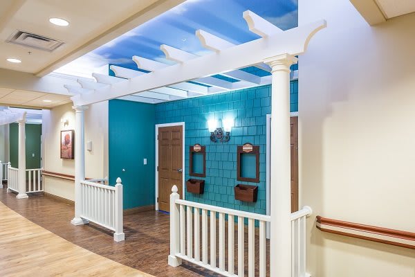 A creatively designed hallway with a turquoise accent wall, white pergola and railing, and warm lighting fixtures.