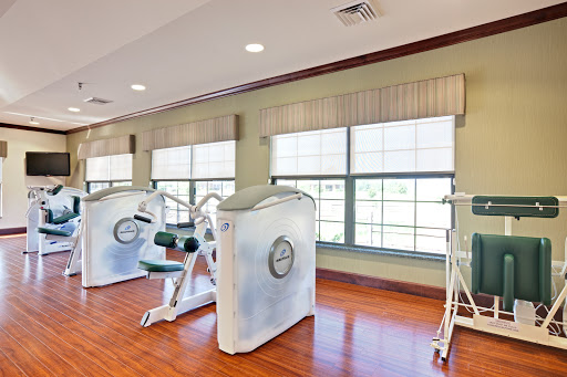 A well-lit gym area featuring strength training equipment and large windows for natural light.