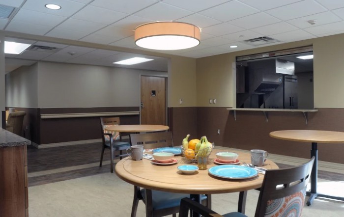 A dining room setup with tables and chairs, featuring a centerpiece of fruits and arranged plates.