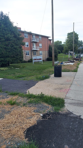 A view of an apartment complex with a sidewalk, grassy area, and a trash can.