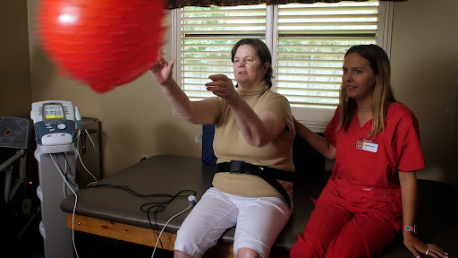 A caregiver assists an elderly woman in a therapy session, promoting physical activity and engagement.