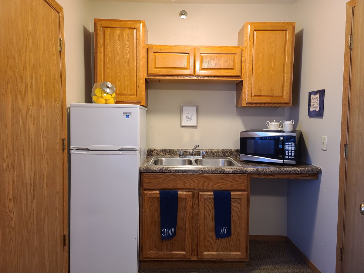 A compact kitchen area with wooden cabinets, a refrigerator, microwave, and sink.