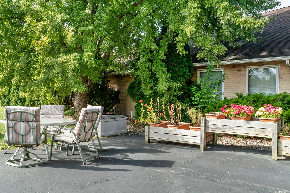 A cozy outdoor patio area surrounded by lush greenery and garden planters, featuring a table and chairs for relaxation.