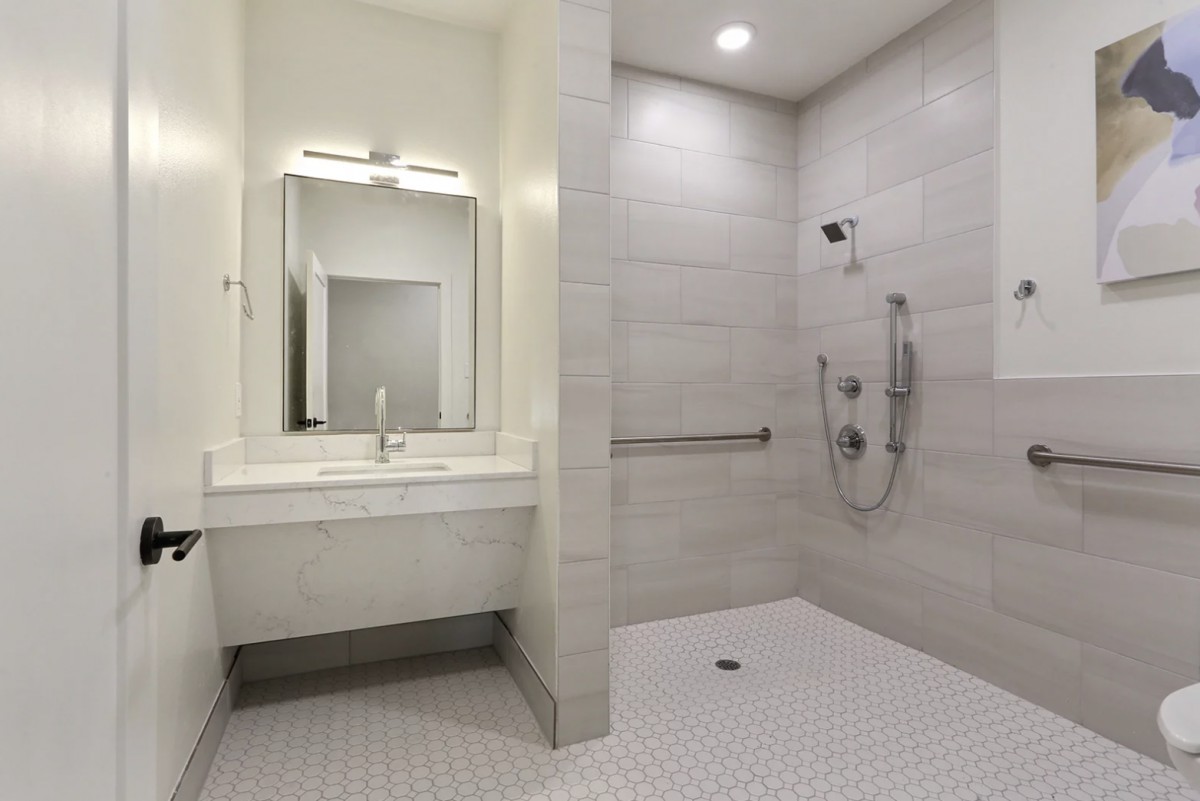 A modern, handicap-accessible bathroom with a tiled shower and sink area.