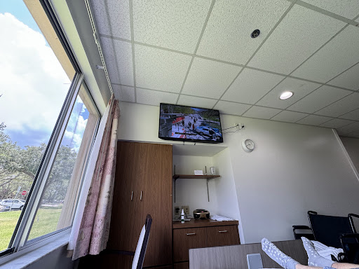 A hospital room featuring a television mounted on the wall and a view through the window.