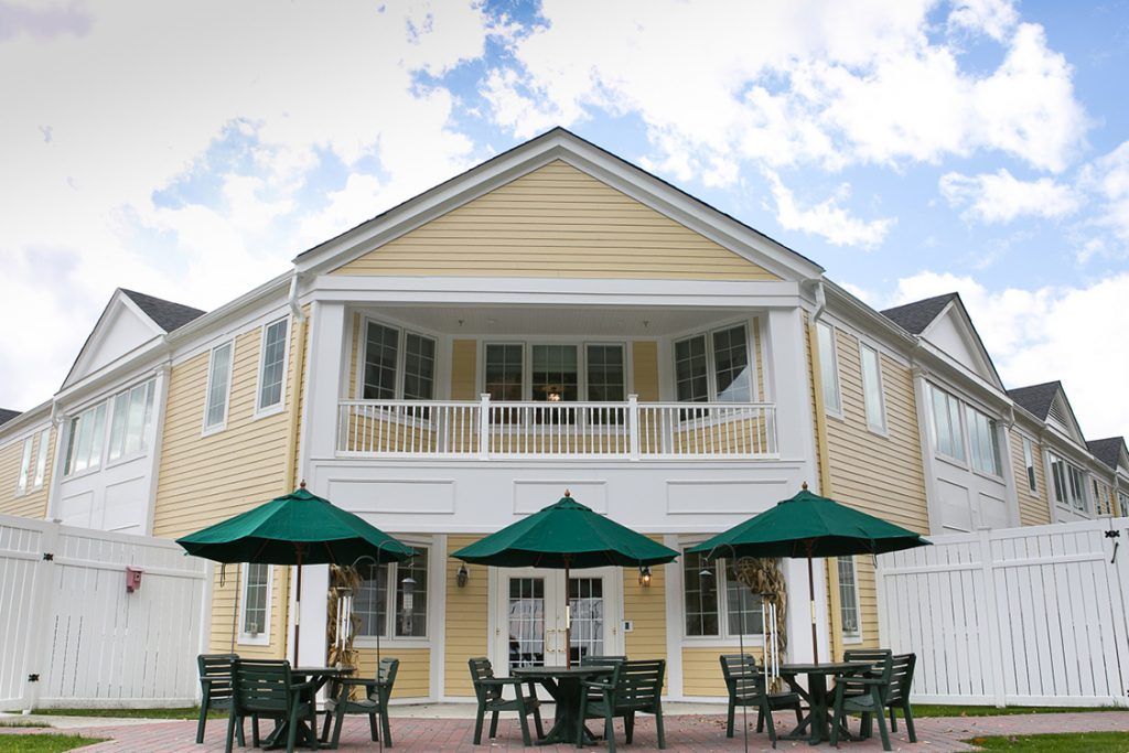A two-story yellow house with a patio and outdoor seating under green umbrellas.