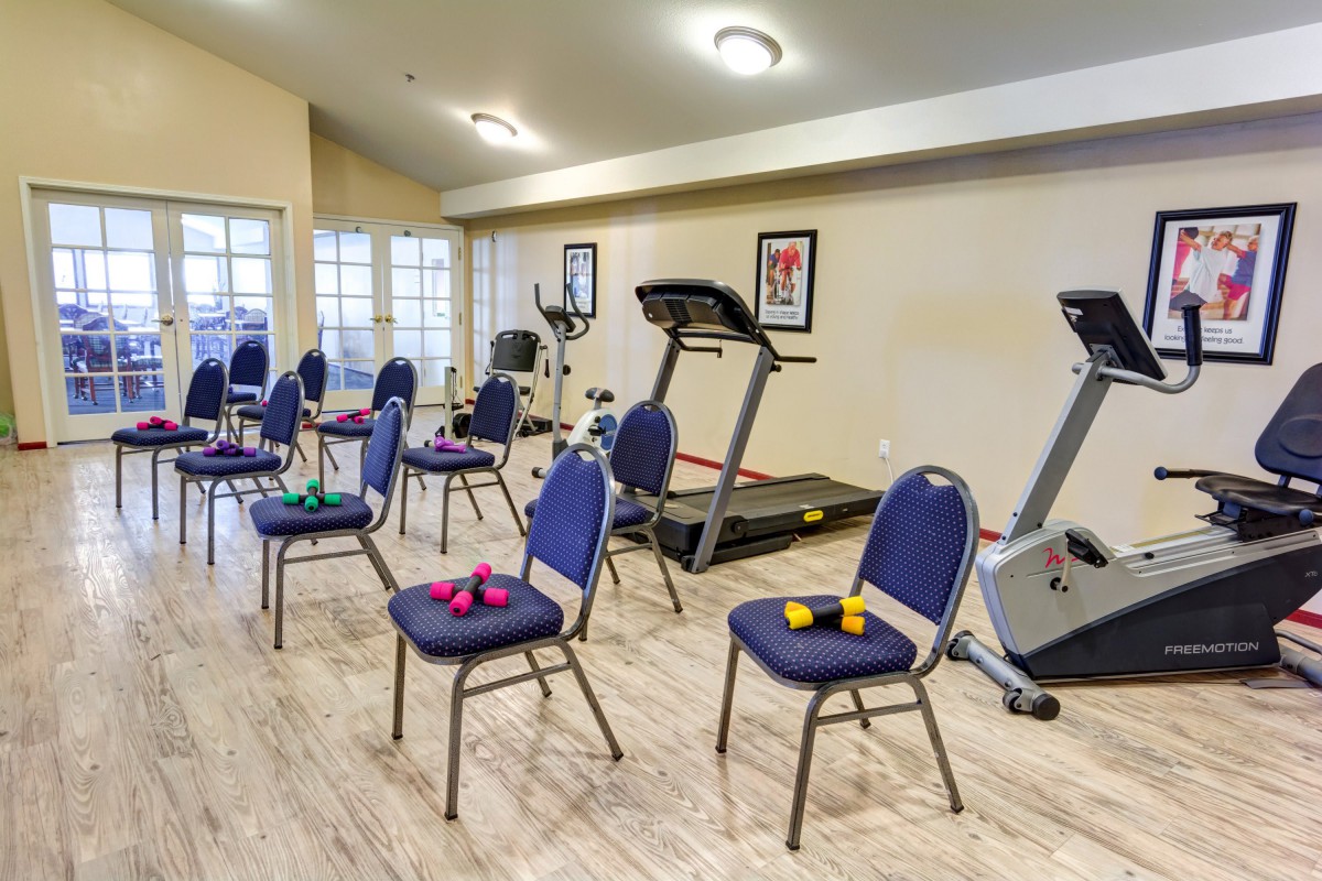 An exercise room with chairs, dumbbells, and treadmills.