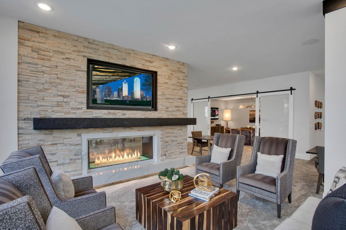 A modern living room with a stone wall and a fireplace under a mounted TV, featuring comfortable armchairs and a stylish coffee table.