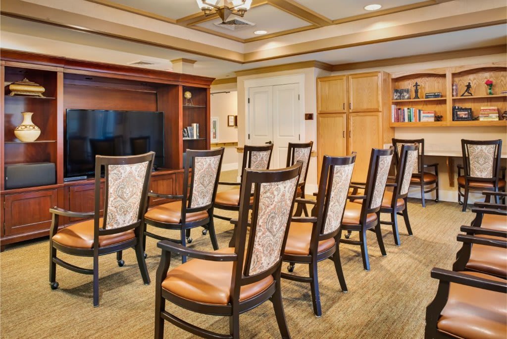 A conference room setup with neatly arranged chairs facing a television, surrounded by wooden furniture and a bookshelf.