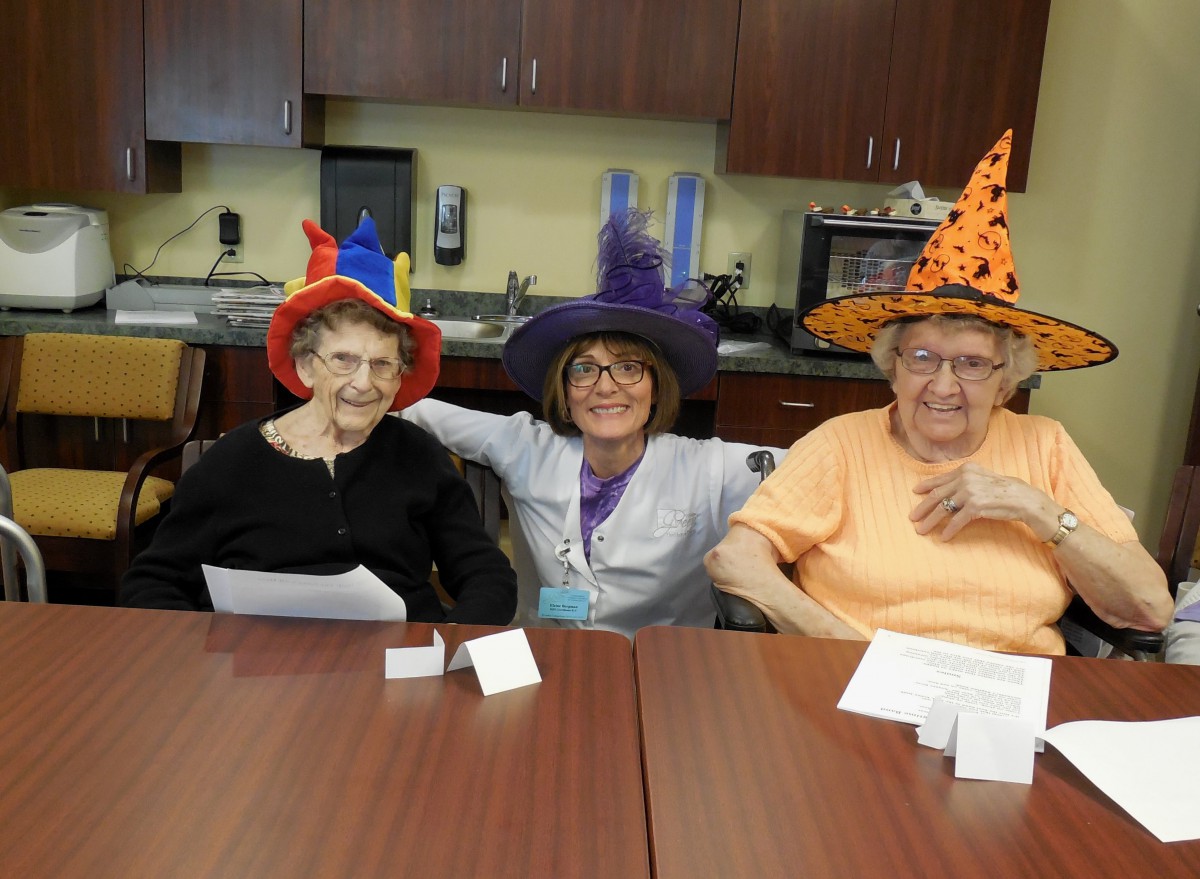Three seniors wearing colorful witch hats celebrate Halloween together.