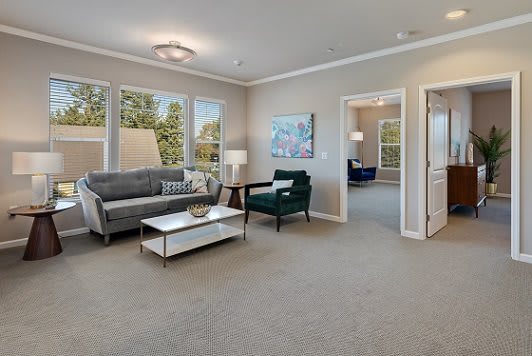 A modern living room with a grey sofa, green armchair, and a sleek coffee table, featuring large windows and neutral decor.