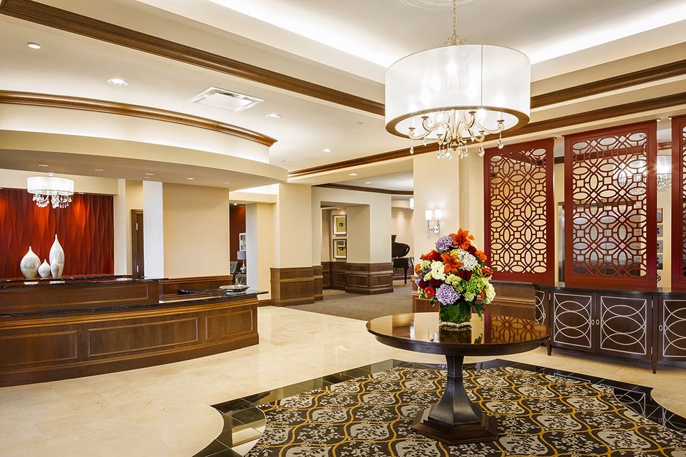 A luxurious hotel lobby featuring elegant decor and a central table with a flower arrangement.