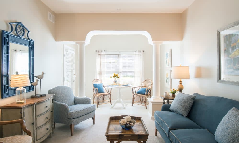 A cozy and elegantly decorated living room featuring a blue sofa, armchairs, a coffee table, and a well-lit window area.