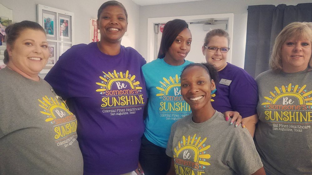 A group of four people wearing colorful t-shirts, smiling indoors.