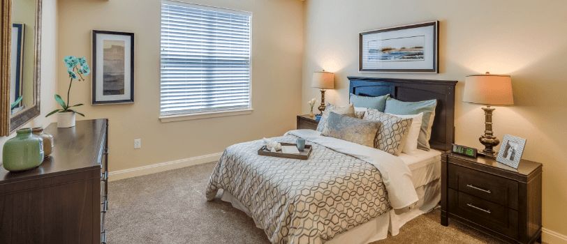 A cozy bedroom with a neatly made bed, soft lighting from a bedside lamp, and framed artwork above the headboard.