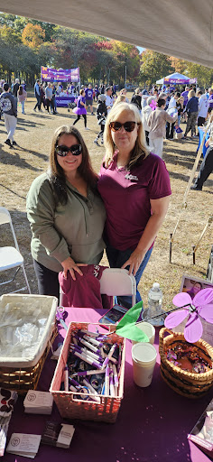 Two women smiling at an outdoor event, posing beside a table with various items.