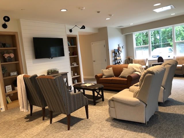 A cozy living room with sofas, armchairs, a TV, and large windows providing natural light.