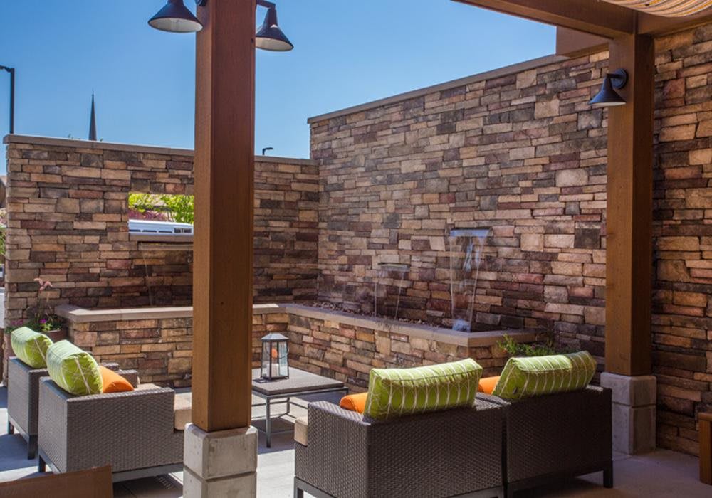 Outdoor patio area with comfortable seating, stone wall, and a fountain.