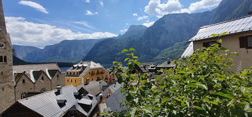 A picturesque view of a village nestled between majestic mountains, showcasing lush greenery and a bright blue sky.