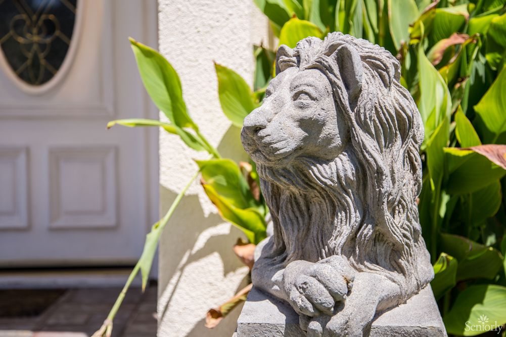 A stone lion statue placed outdoors, surrounded by plants.