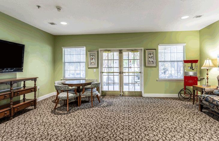 A cozy room with green walls, a round table with chairs, and large windows providing natural light.