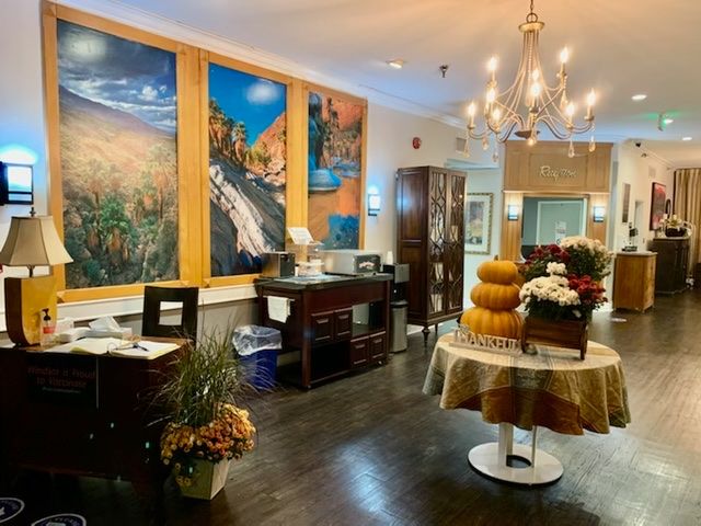 A cozy restaurant interior adorned with vibrant paintings and elegant decor, featuring a chandelier and seasonal decorations including pumpkins and flowers.