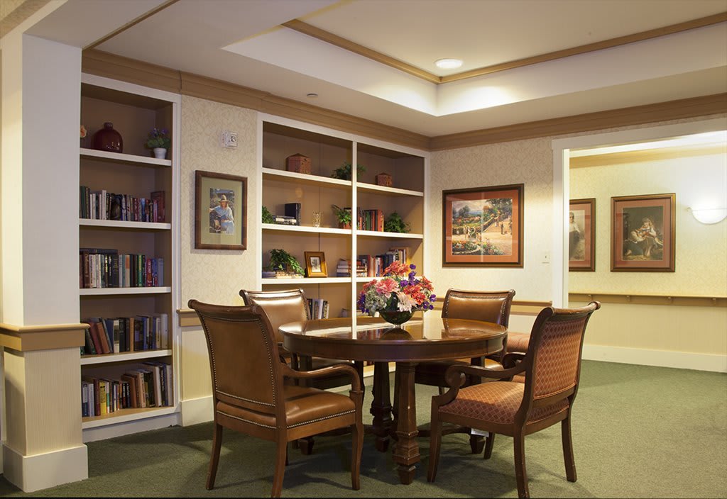 A cozy library corner with a round table surrounded by chairs and filled with bookshelves.